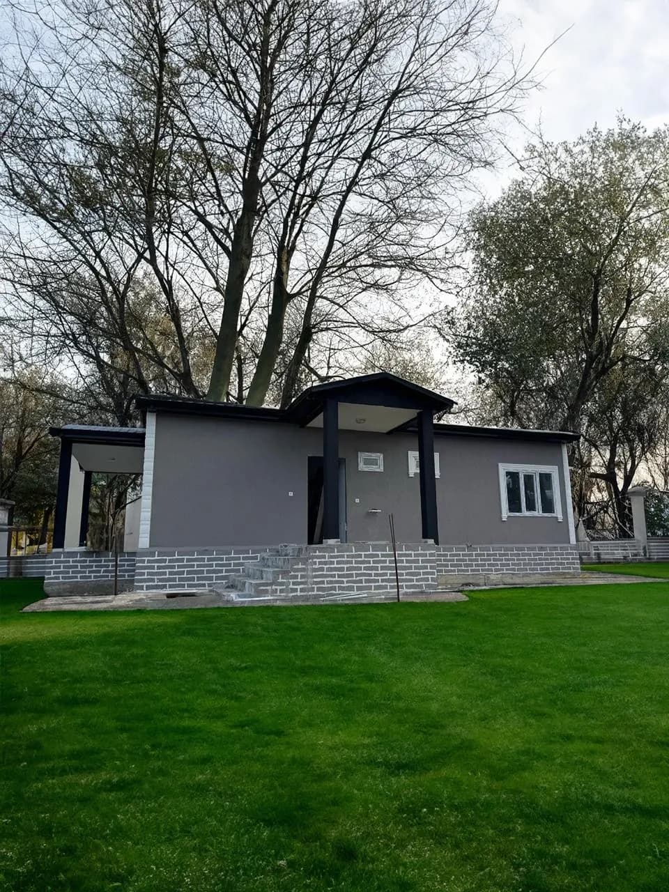 Gri cepheli, siyah kolonlu girişi olan tek katlı prefabrik ev