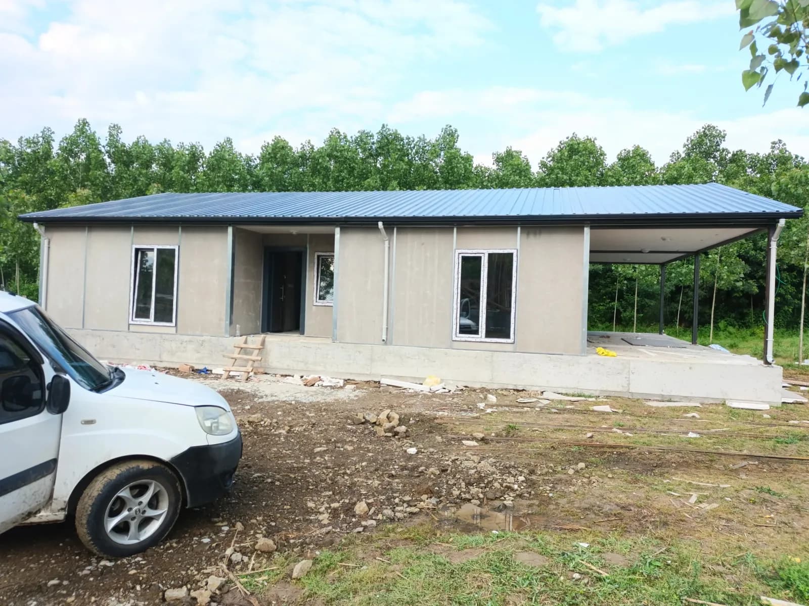 Mavi çatılı, verandalı tek katlı prefabrik ev ve montaj sahası