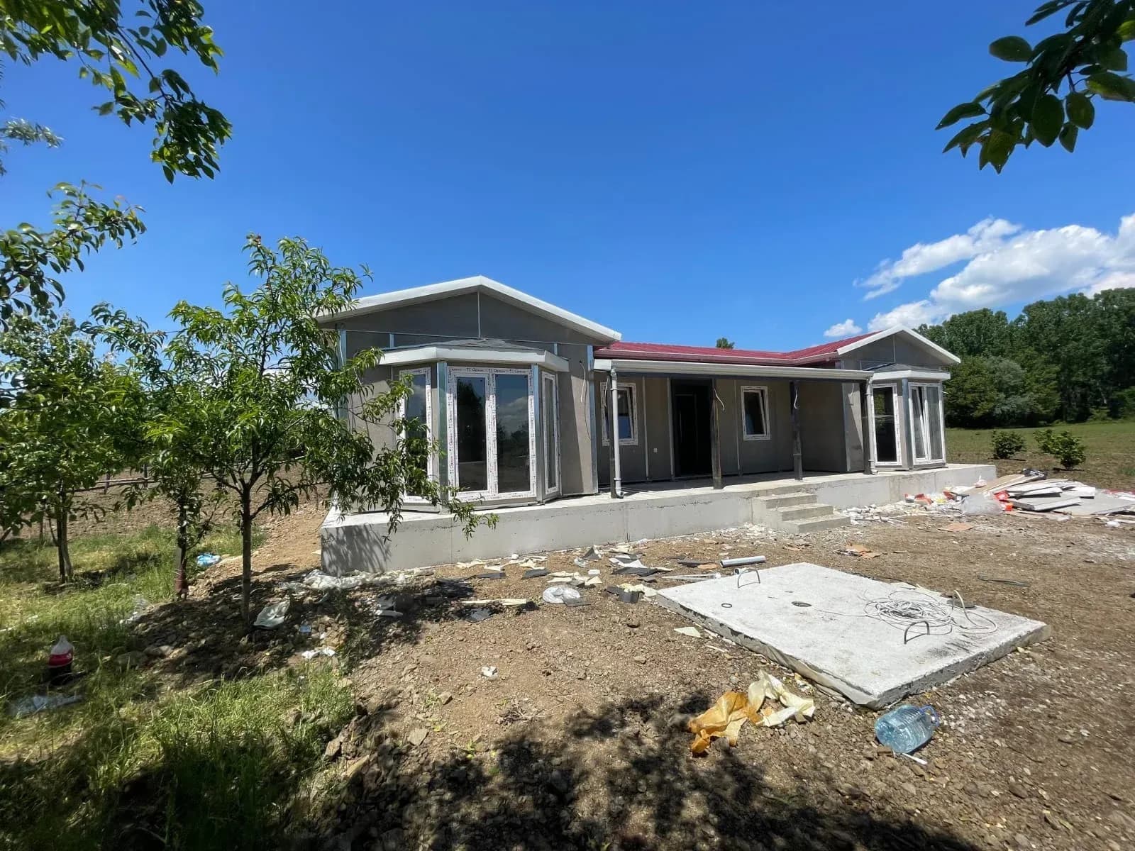Kırmızı çatılı, gri cepheli tek katlı prefabrik ev ve bahçesi